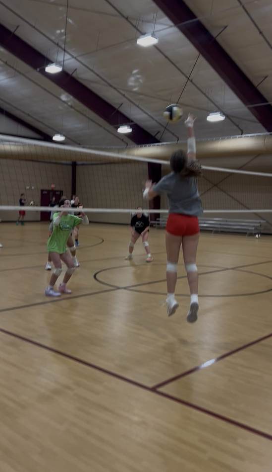 An athlete rises for a swing at the net during an indoor practice rally