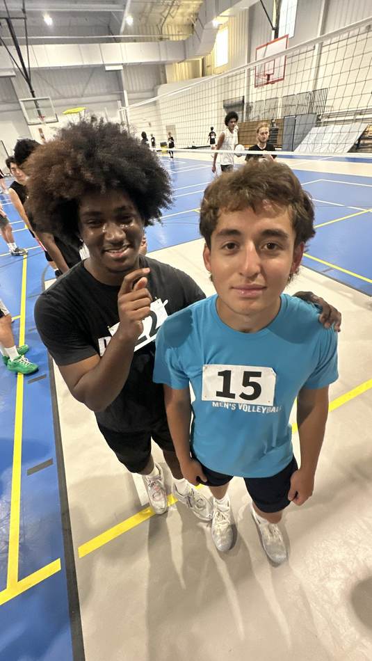 Two athletes courtside at a men's volleyball tournament between matches
