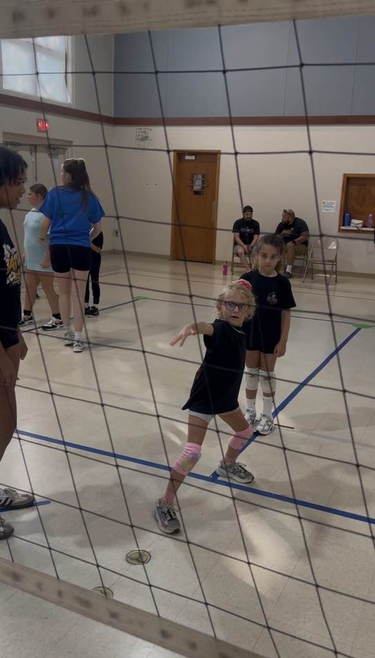 A young athlete in defensive stance during a beginner session, seen from behind the net