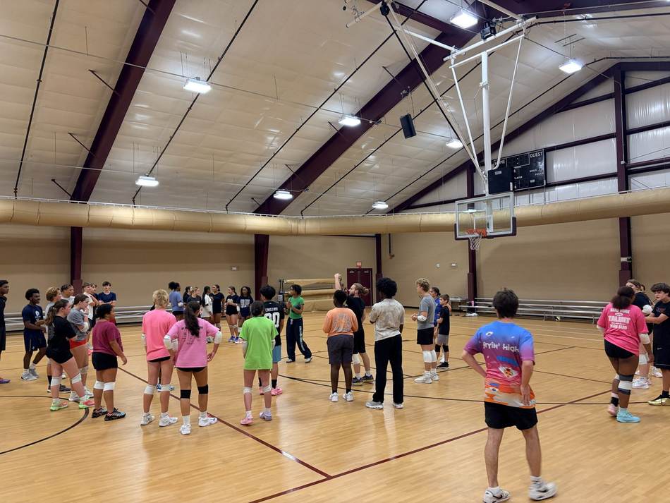 A large group of athletes circled up on the court at the start of practice